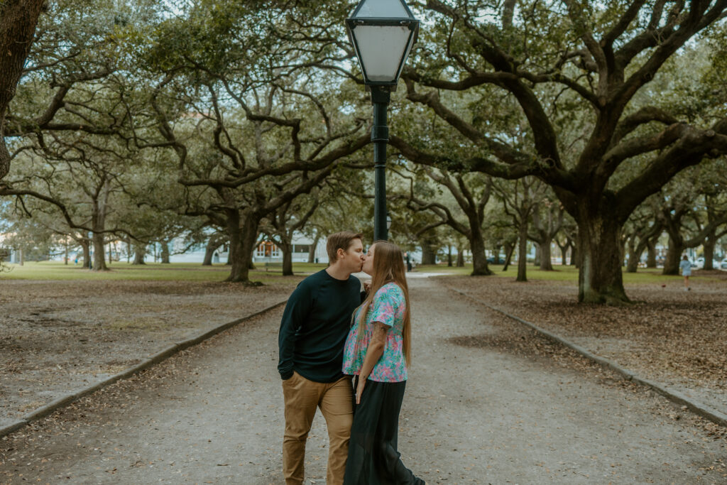 A couple posing on a cobblestone street in downtown Charleston, surrounded by pastel-colored historic homes and lush greenery, captured during a romantic photo session.