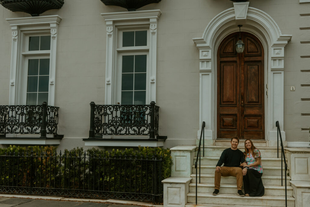 A stunning image of a couple standing in front of a grand historic mansion in downtown Charleston, featuring elegant architecture, tall columns, and a lush, manicured garden.