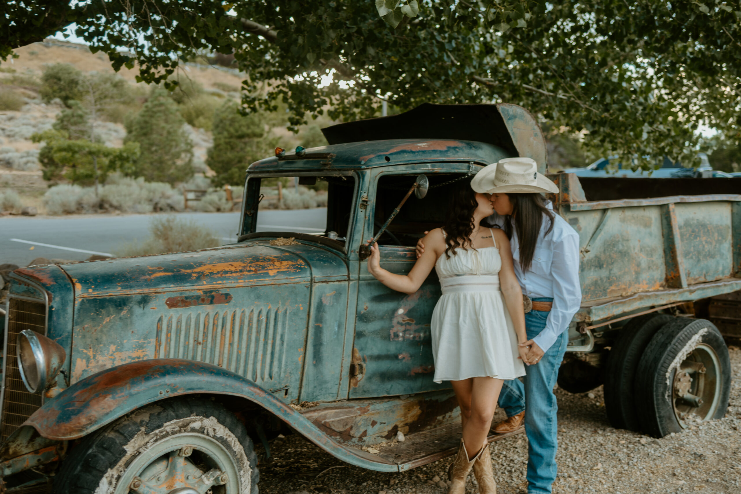 A joyful couple standing by their vintage truck, smiling warmly at each other, captured in the golden Arizona sunset. The truck's rustic charm complements the desert landscape, making this moment perfect for a Tucson wedding photographer's portfolio.