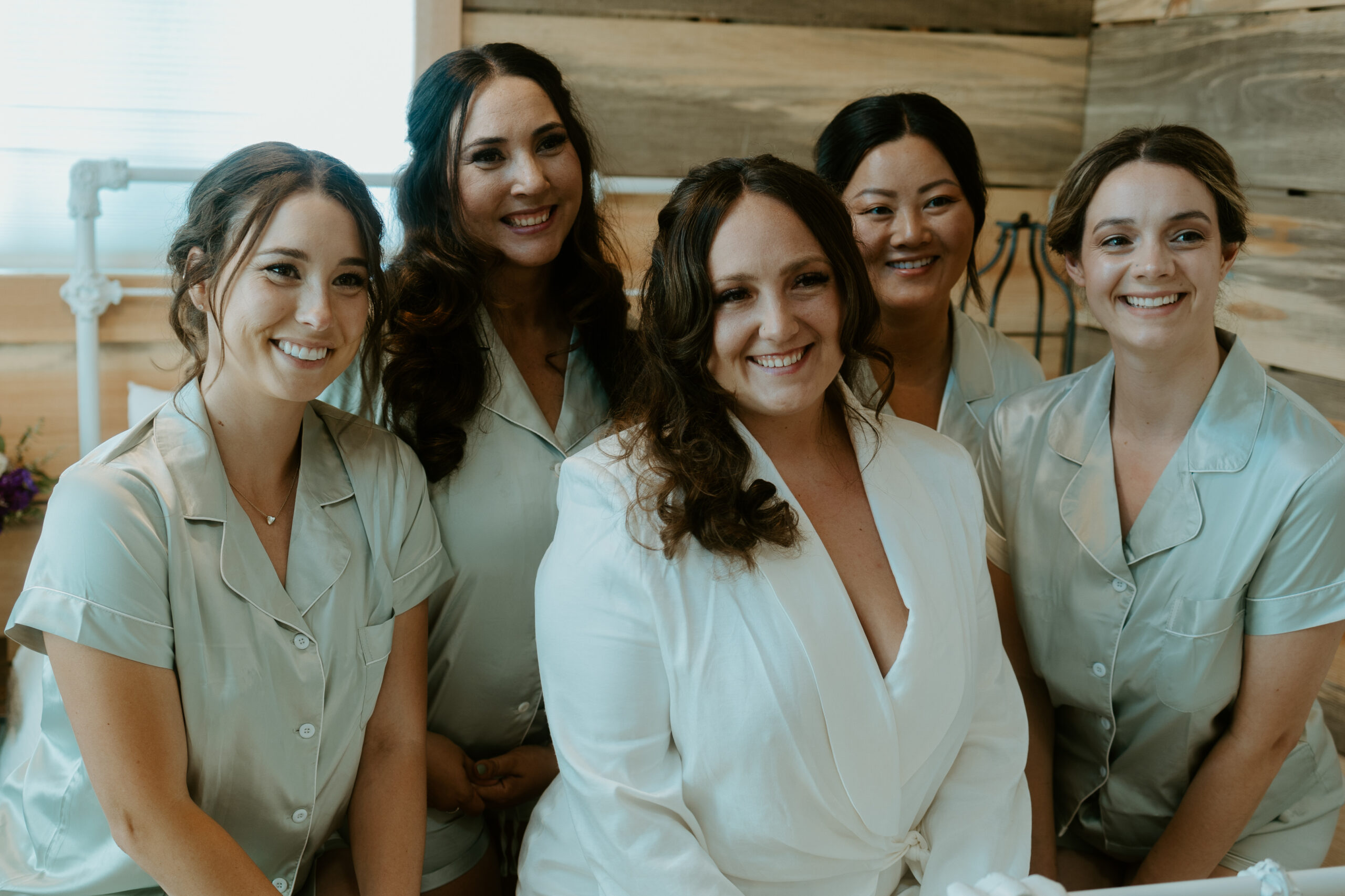 A radiant bride surrounded by her bridesmaids, all smiling and sharing a joyful moment under the Tucson sun. Their elegant dresses and the natural desert backdrop create a timeless image, perfect for showcasing the connection and love of the bridal party. Captured by a Tucson wedding photographer.