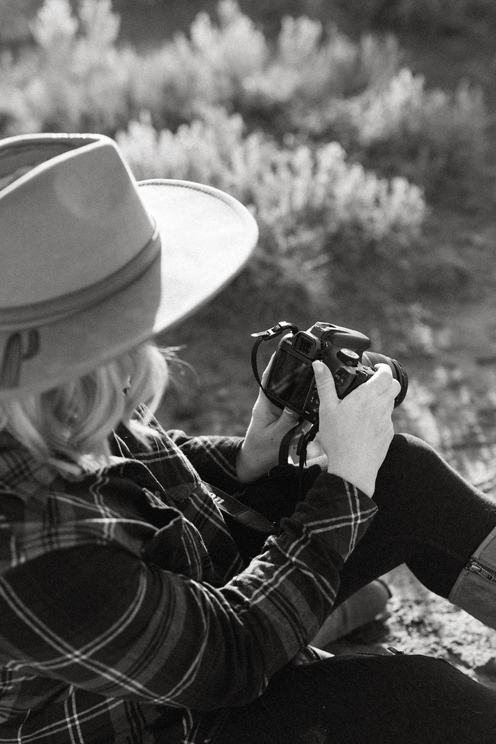 Anne Byrd, a luxury wedding photographer, holding her camera with a confident smile, ready to capture timeless moments. Photographed in a natural outdoor setting with soft, warm lighting.